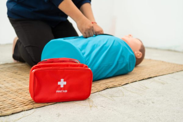 A woman studies at a gas station  an adult CPR dummy on the floor.practices situation assessment