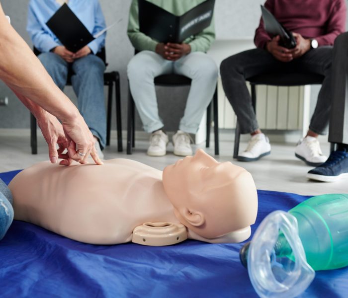 Close-up of female instructor using mannequin on floor to teach cardiopulmonary resuscitation at training class