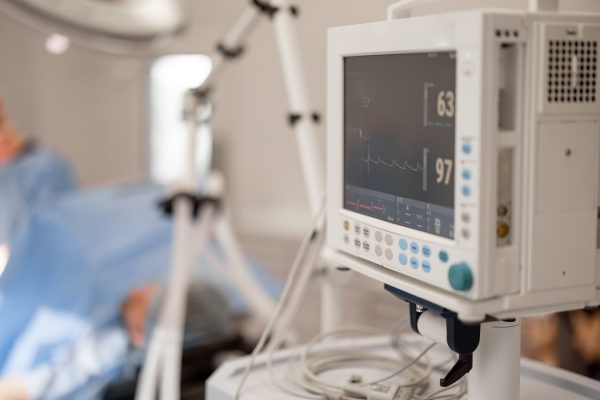 Surgery treatment in progress. Heart rate monitor on a foreground and surgeons working behind. Concept of monitoring the patient's condition during surgery